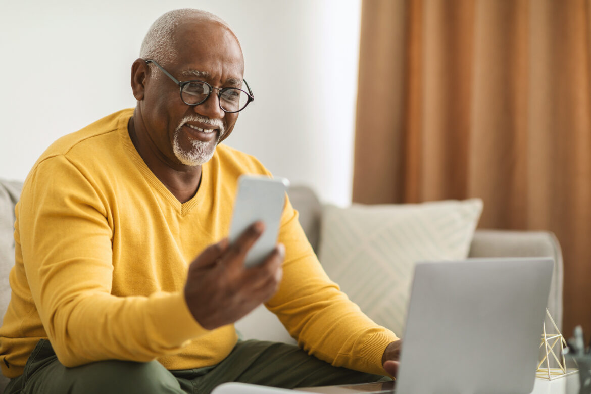 Senior Black Man Using Smartphone And Laptop Working Online Indoors